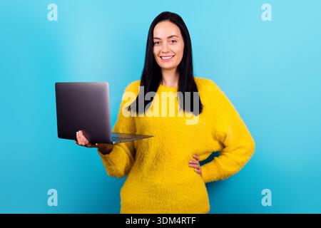 Portrait photo de femme d'affaires gardant l'ordinateur portable souriant dans le pull moelleux jaune isolé fond de couleur bleue Banque D'Images