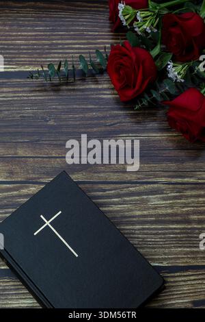 Sainte Bible avec croix et roses rouges sur fond de bois Banque D'Images