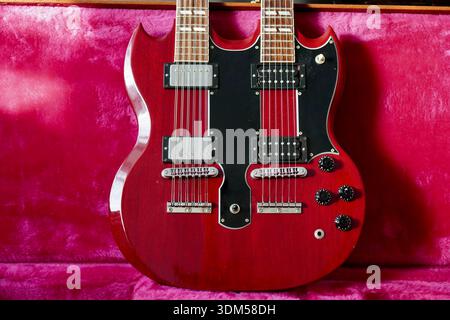 Guitare rouge à double cou emblématique dans son étui en peluche rose. La lumière brille sur le côté gauche du corps révélant le contour. Banque D'Images