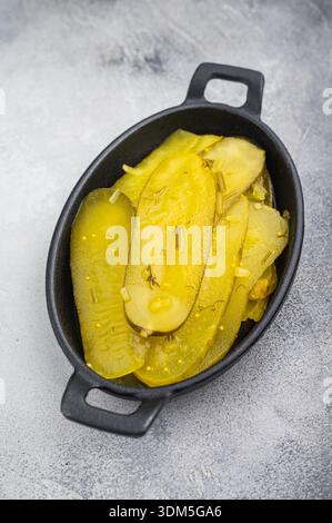Tranches de concombre mariné rustique dans un plat en fonte avec de l'ail et des épices sur fond clair texturé, nourriture jaune saumurée vibrante Banque D'Images