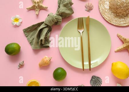 Belle table avec assiette, couverts dorés, serviette et agrumes sur fond rose Banque D'Images