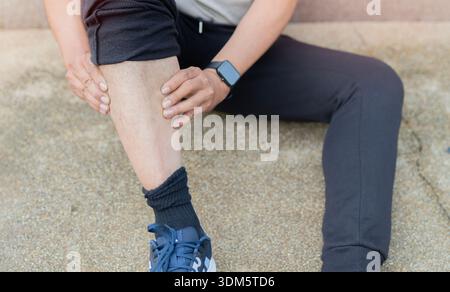 Vue en angle élevé de l'homme après l'entraînement de fitness et le jogging se trouve sur le sol et souffre de douleurs aux jambes, massages les muscles des jambes Banque D'Images