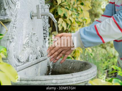 Mains attrapant l'eau d'un vieux style de robinet dans le jardin. Mains tournant sur un robinet à l'extérieur, l'eau coule. Banque D'Images