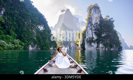 Un voyageur se détend sur un bateau traditionnel en bois, entouré de falaises de calcaire à couper le souffle et de verdure luxuriante dans le parc national de Khao Sok, en Thaïlande. Th Banque D'Images