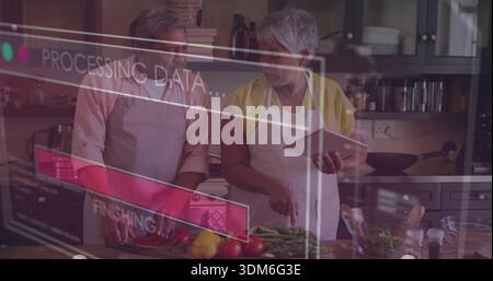 Cuisinant couple senior portant tabliers hachant des tomates au comptoir de la cuisine, consultant tablette HUD Banque D'Images
