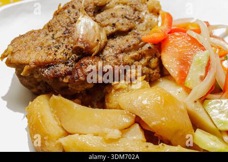 Gros plan de viande de porc rôti appétissante avec pommes de terre et salade sur une assiette. Repas copieux. Gros plan sur la viande de porc rôtie appétissante avec pommes de terre et Banque D'Images