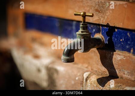 Un robinet vieilli en laiton et en métal dépasse d'un mur en terre cuite altérée avec une bande décorative de tuiles bleues à Séville, Andalousie, Espagne, capturé wi Banque D'Images