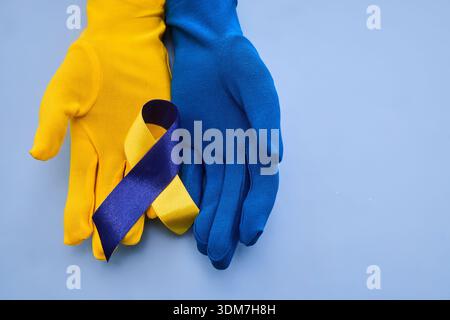 Gants jaunes et bleus tenant le ruban de sensibilisation au syndrome Banque D'Images