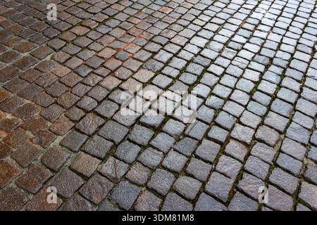Texture pavée humide avec motif de pierre naturelle et mousse entre les fissures créant une atmosphère historique urbaine. Banque D'Images