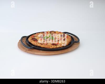 Pizza saucisse et tomate dans une poêle en fonte sur planche de bois isolé sur blanc Banque D'Images