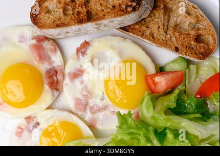 Petit déjeuner d'oeufs frits avec bacon, salade mixte et pain grillé.Une assiette avec oeufs frits, une portion de légumes et une baguette croustillante dans une restaura Banque D'Images