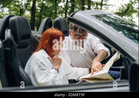 Conception touristique, avec une carte. Couple senior conduisant une voiture cabriolet convertible. Banque D'Images
