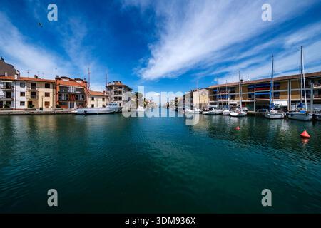Vue le long du Porto Canale à Grado avec des bateaux amarrés et des bâtiments historiques sous un ciel bleu. Banque D'Images