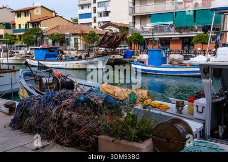 Filets de pêche sur le quai de Porto Canale à Grado avec des bateaux de pêche bleus traditionnels et des bâtiments résidentiels. Banque D'Images