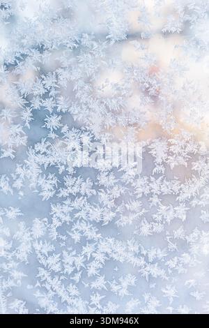 Un fond de motifs de flocon de neige et de cristaux de givre sur une fenêtre. Vitrage givré baigné de lumière du soleil orange sur fond de tons bleus froids. Banque D'Images