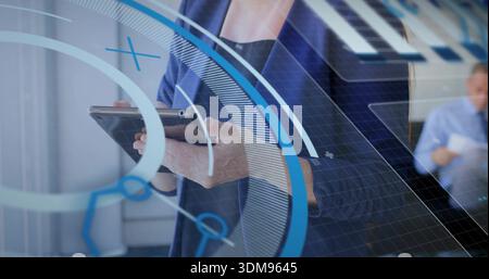 Tenant la femme dans le blazer marine interagissant avec la tablette au bureau, l'homme lisant des documents, les superpositions HUD Banque D'Images