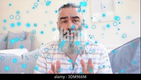 Homme barbu parlant dans la chemise rayée geste sur le canapé dans le salon avec des superpositions hexagonales bleues Banque D'Images