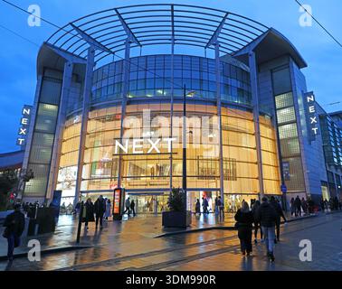 Illuminé le PROCHAIN grand magasin au crépuscule en hiver, à l'extérieur de Manchester Arndale près de Exchange Square, centre-ville de Manchester, Angleterre, Royaume-Uni, avec des acheteurs Banque D'Images