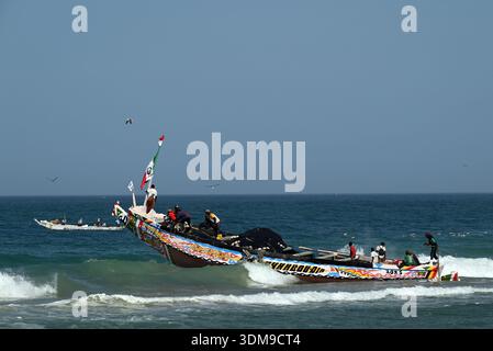 Un bateau de pêche traditionnel quittant la plage à travers les vagues à Nouakchott, Mauritanie. Banque D'Images