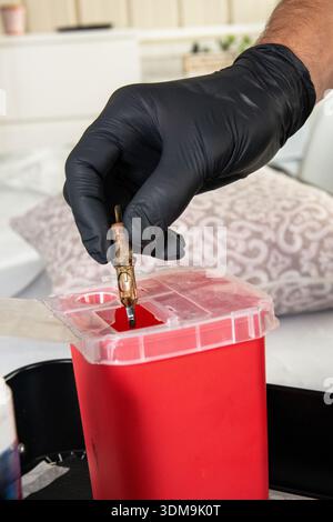 Main dans le gant jetant l'aiguille de tatouage dans le récipient pour objets pointus et tranchants Banque D'Images