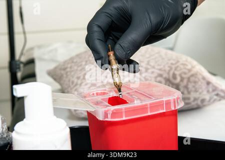 Tatoueur se débarrassant de la cartouche d'aiguille usagée dans un récipient pour objets pointus et tranchants Banque D'Images