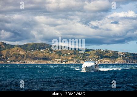 Petit bateau à moteur naviguant sur la mer ouverte avec des montagnes lointaines et ciel nuageux créant un paysage de voyage pittoresque. Banque D'Images