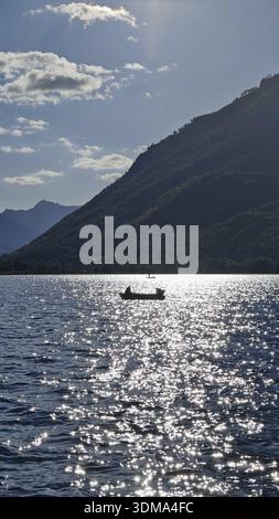 Un bateau solitaire sur un lac étincelant avec des montagnes en arrière-plan et une atmosphère ensoleillée, le lac Plav, Monténégro Banque D'Images