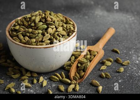Bol et cuillère en bois avec épice de cardamome sur fond noir, gros plan Banque D'Images