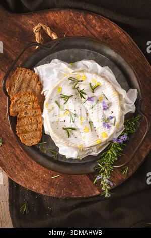 Un plan rustique de haut en bas de camembert fondu garni de romarin frais, d'huile d'olive et de lavande. L'éclairage chaud et sombre souligne le texte crémeux Banque D'Images