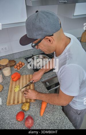 Homme tranchant du gingembre frais et des légumes sur une planche à découper en bois pour un repas sain Banque D'Images