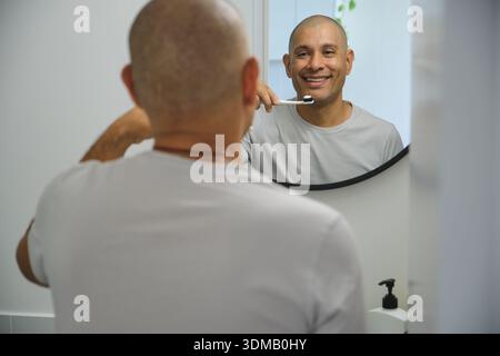 Homme se brossant les dents devant un miroir de salle de bain, en se concentrant sur l'hygiène bucco-dentaire Banque D'Images