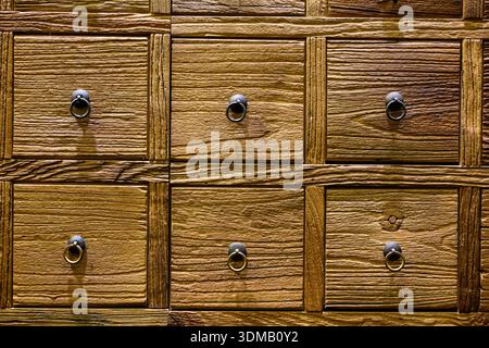 Une armoire à pharmacie chinoise traditionnelle en bois dans un ton brun chaud se dresse avec ses nombreux petits tiroirs carrés disposés dans un ordre parfait. Banque D'Images