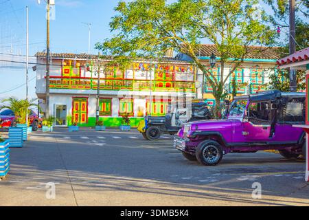 Une scène vibrante avec une jeep vintage violette et des bâtiments colorés de style colonial sous un ciel bleu clair. Banque D'Images