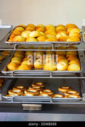 Une vue rapprochée de pâtisseries colombiennes dorées empilées sur des plateaux métalliques, présentant différentes formes et textures. Banque D'Images