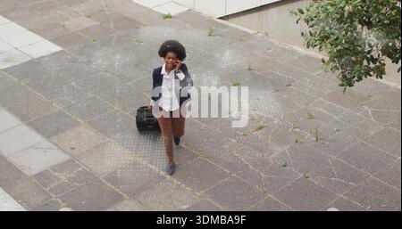 Femme qui marche tirant la valise noire tenant le téléphone à plaza Blazer sac tactile-points dalles mauvaises herbes Banque D'Images