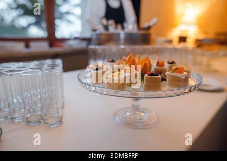 Une sélection de délicats amuse-gueules et canapés sont magnifiquement disposés sur un plateau en verre à plusieurs niveaux, prêt pour les invités lors d'un événement Banque D'Images