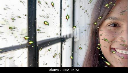 Femme souriante penchée par la fenêtre noire encadrée de métal à la maison, dans le dessus sombre, les étincelles vertes, l'espace de copie Banque D'Images