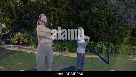 Étirer deux femmes asiatiques faisant des étirements de bras sur des tapis noirs dans le jardin, portant des vêtements de sport Banque D'Images