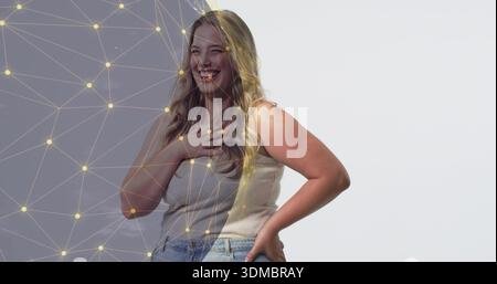 Femme souriante portant un haut beige, un Jean debout dans un fond gris ou blanc de studio, une superposition de réseau Banque D'Images