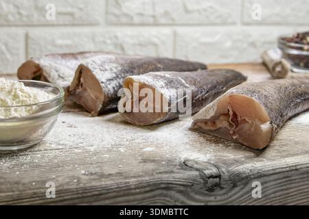 Filets de poisson crus saupoudrés de farine disposés sur une table en bois avant la cuisson Banque D'Images