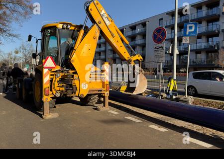 Poznan, Pologne - 18 novembre 2025 : chargeuse-pelleteuse jaune avec pelle près du pipeline violet, montrant les travaux de génie civil et le développement vital des services publics urbains Banque D'Images