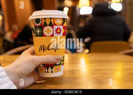 Poznan, Pologne - 19 novembre 2025 : une main de personne saisit une tasse de café McCafe au design festif vibrant, en dégustant une boisson chaude dans un R détendu Banque D'Images