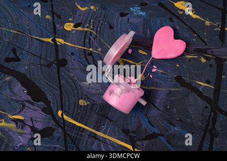 Plat vibrant avec coeur rose miniature émergeant d'un pot de peinture rose vif au milieu d'un fond tourbillonnant inspiré de la galaxie avec des accents dorés. Banque D'Images