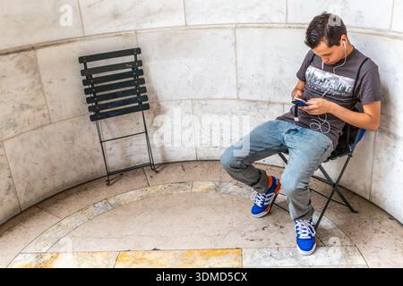 Dans une alcôve extérieure de la New York public Library, un jeune homme est assis à vérifier son téléphone portable. Banque D'Images