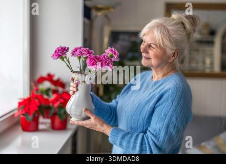 Femme âgée tenant un vase de fleurs à la maison Banque D'Images