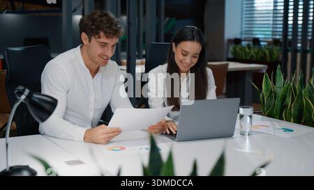 Deux heureux rire femme d'affaires caucasienne et homme travaillant ensemble avec des papiers rire humoristique ridicule collègues sourire avec des documents et un ordinateur portable Banque D'Images