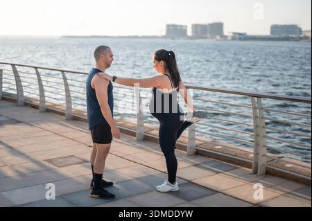 Un couple participe à une séance d'étirements au bord de l'eau, montrant leur engagement envers la forme physique et la santé tout en chérissant leurs moments spéciaux t Banque D'Images
