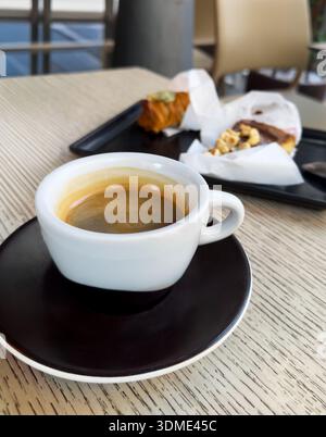 Petite tasse brune d'espresso sur une soucoupe avec des desserts en arrière-plan sur la table. Plat savoureux et rapide à préparer. Concept d'italien traditionnel Banque D'Images