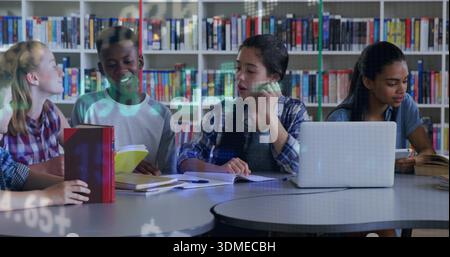 Assis les élèves dans des vêtements décontractés discutant du travail scolaire à la bibliothèque de l'école, avec un ordinateur portable et des livres Banque D'Images