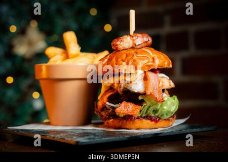 Un grand hamburger au bacon et à la laitue se trouve sur une assiette à côté d'un petit bol de frites. Le hamburger est surmonté d'un cure-dent, et les frites sont dans une casserole Banque D'Images